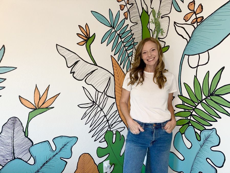 Lindsey Colwill standing in front of a tropical line-art wall she painted